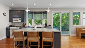 A modern kitchen with a central island, dark cabinetry, and a view of greenery through large windows. - Luxury Lakefront Escape | 6 Bedrooms & Pet Friendly (West Olive)