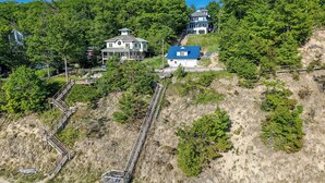 A coastal property with a staircase leading to a beach, surrounded by dense forest and a large house with a blue roof. - Luxury Lakefront Escape | 6 Bedrooms & Pet Friendly (West Olive)