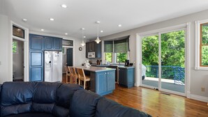 A modern kitchen with blue cabinets, a central island, and a dining area with wooden chairs. - Luxury Lakefront Escape | 6 Bedrooms & Pet Friendly (West Olive)