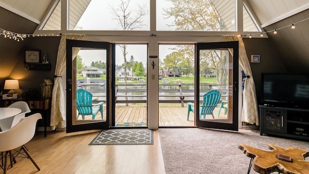 Een ruime woonkamer met een grote schuifpui die leidt naar een terras, een televisie en een zithoek met stoelen.
