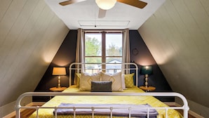 Een slaapkamer met een stapelbed, een raam met gordijnen, een plafondventilator en een lamp op een nachtkastje.