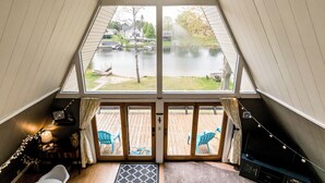 Een kamer met een groot raam met uitzicht op een meer, een houten terras buiten en een gezellig interieur met een bank en een televisie.
