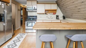 Een moderne keuken met roestvrijstalen apparatuur, een houten kookeiland met barstoelen en een wand bekleed met hout.