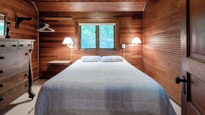Un dormitorio con paneles de madera, una cama, un aparador y dos lámparas fijadas a la pared.