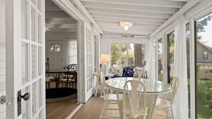 A conservatory with a glass table and chairs, a door leading to a room, and a view of the outside.