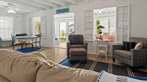 A spacious room with a bed, a dining table with chairs, a sofa, and a chair. There is a sign that reads 'WELCOME TO THE BEACH.'