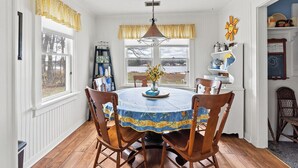 A dining room with a round table, wooden chairs, a chandelier, and a view of the outdoors. - Charming 2-Bedroom Strong Cottage in Twin Lake, MI (Twin Lake)