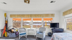 A room with two beds, a television, a fan, and a window with a view of a snowy landscape. - Charming 2-Bedroom Strong Cottage in Twin Lake, MI (Twin Lake)