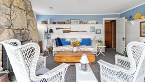 A cozy living room with wicker chairs, a wooden coffee table, and a blue and white patterned sofa. - Charming 2-Bedroom Strong Cottage in Twin Lake, MI (Twin Lake)