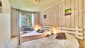 Un dormitorio con dos camas, paredes de paneles de madera y una pared de piedra visible a través de una ventana, además de un cuadro pequeño en la pared.