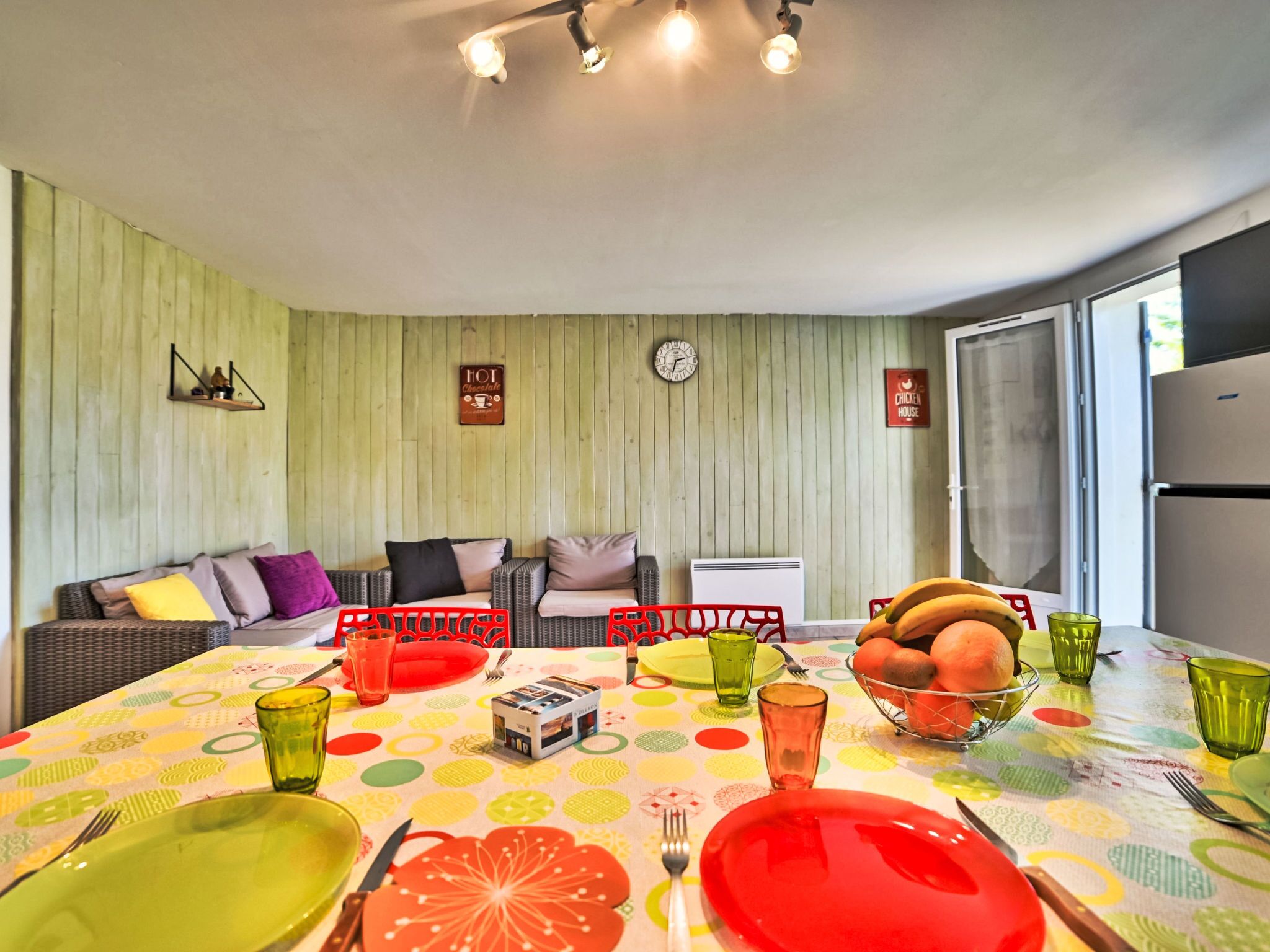 A dining area with a table set for four, a sofa, a clock, and a refrigerator.