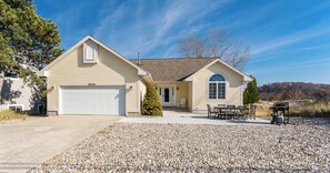 A two-story house with a garage, a covered patio, and a gravel driveway.