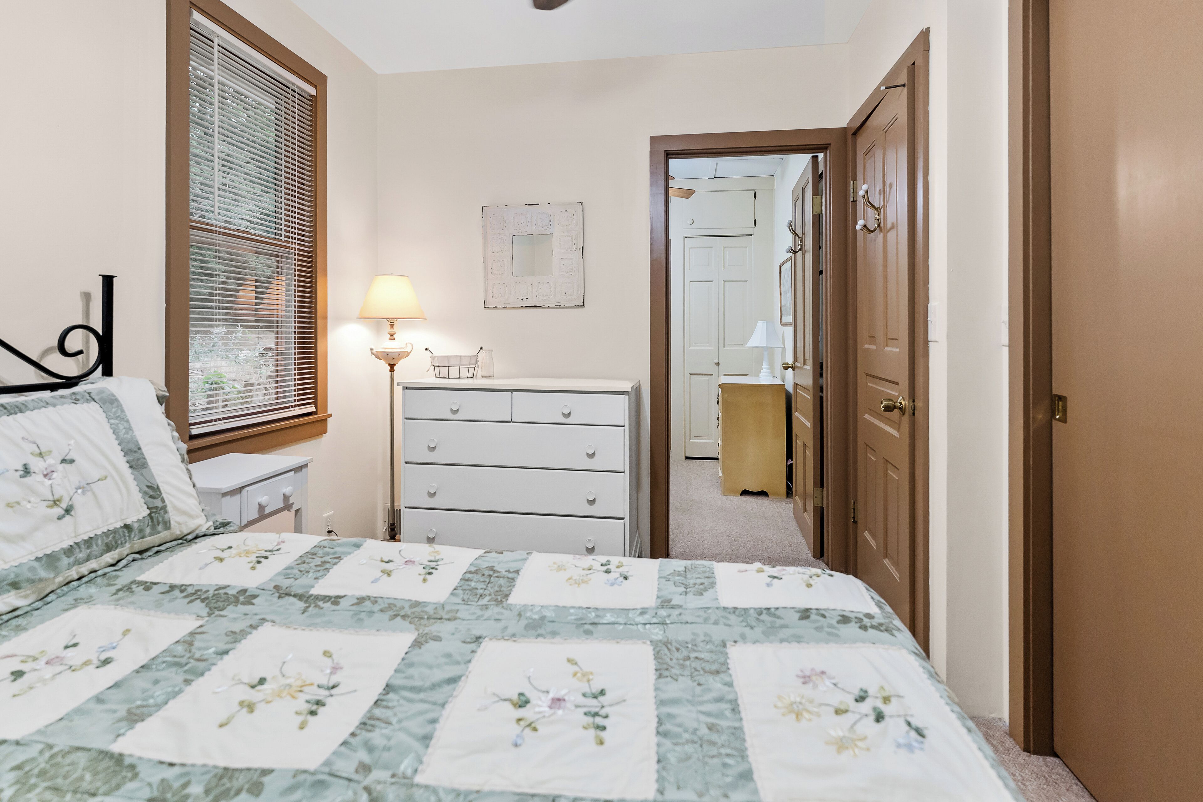 Un dormitorio con cama, cómoda, lámpara y una puerta que da a otra habitación.