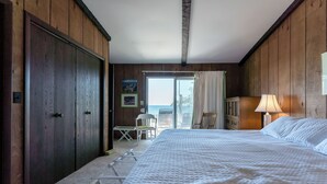Un dormitorio con una cama grande, un armario de madera, una silla, una mesita y vistas al mar a través de una puerta corrediza.