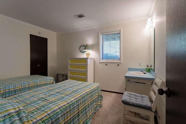 A bedroom with two beds, a dresser, a chair, a window with blinds, a mirror, and a sink. - Beachfront cottage on North Shore Grand Haven (Spring Lake)