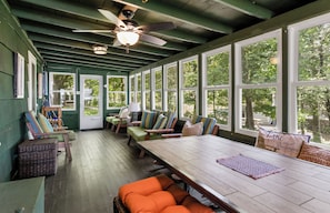 A covered porch with wooden benches, a table, and a ceiling fan.