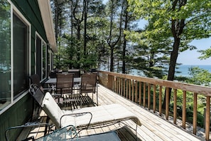 A wooden deck with outdoor furniture, overlooking a body of water and surrounded by trees.