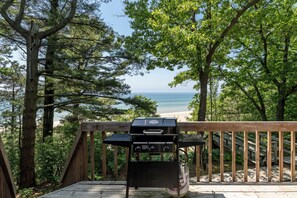 A grill on a wooden deck with a view of the ocean.