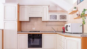 Una cocina con muebles blancos, horno empotrado, microondas y cafetera.