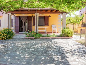 A covered outdoor seating area with a table and chairs, a stone pathway, and a building entrance with shutters. - Apartment Remo by Interhome (Budoni)