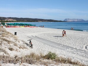 A beach with a bicycle path, beach umbrellas, and a few people. - Apartment Remo by Interhome (Budoni)