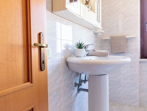 Une salle de bain avec une porte en bois, un lavabo blanc, une serviette et une plante.
