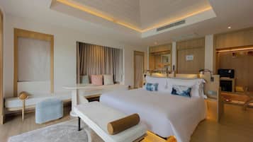 A modern hotel room with a large bed, a sitting area with a bench, a small table, and a wardrobe.