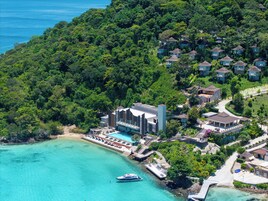 A resort with multiple bungalow-style accommodations surrounded by lush greenery, a swimming pool, and a dock with a boat.
