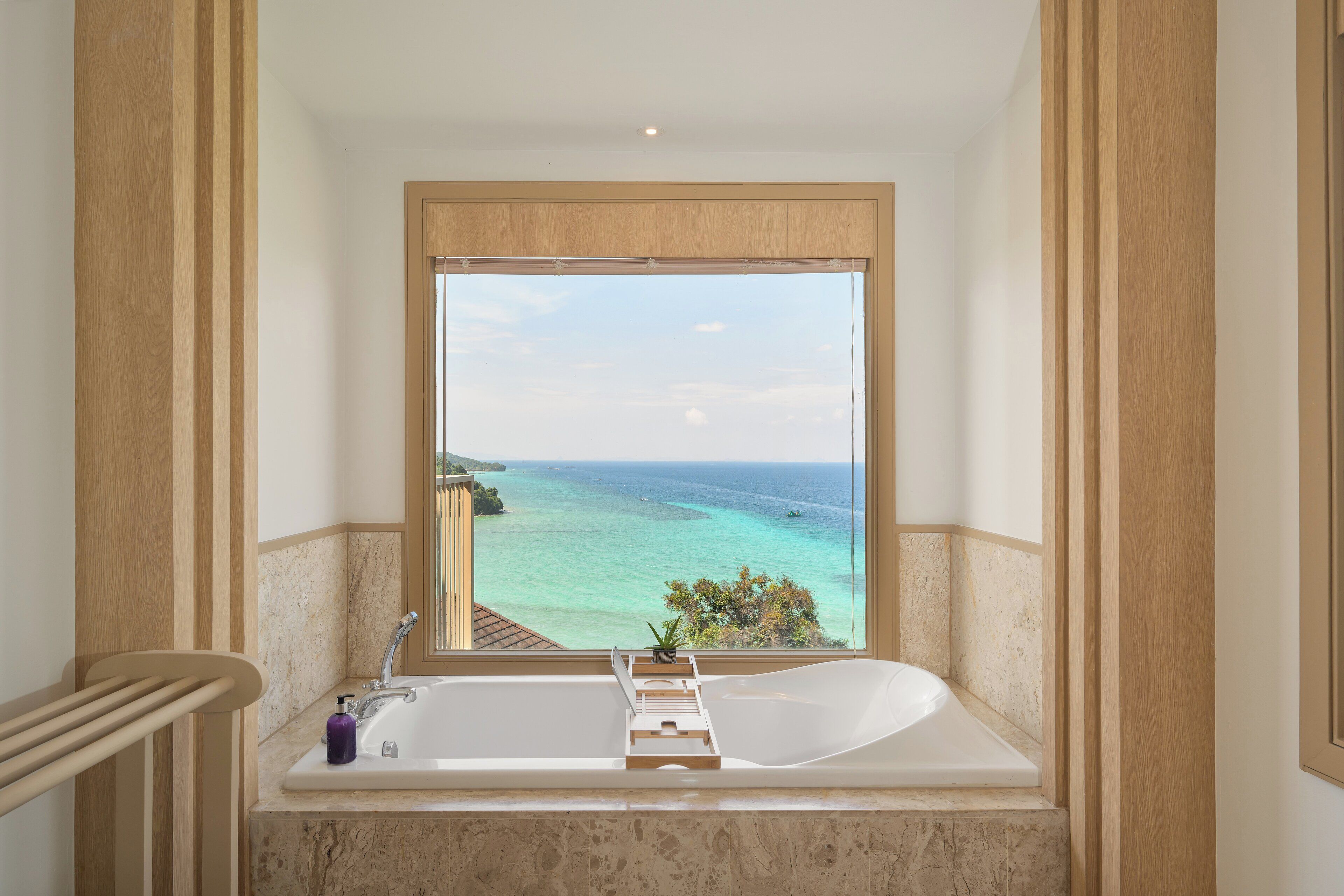 Un baño con bañera, ventana y vista al océano.