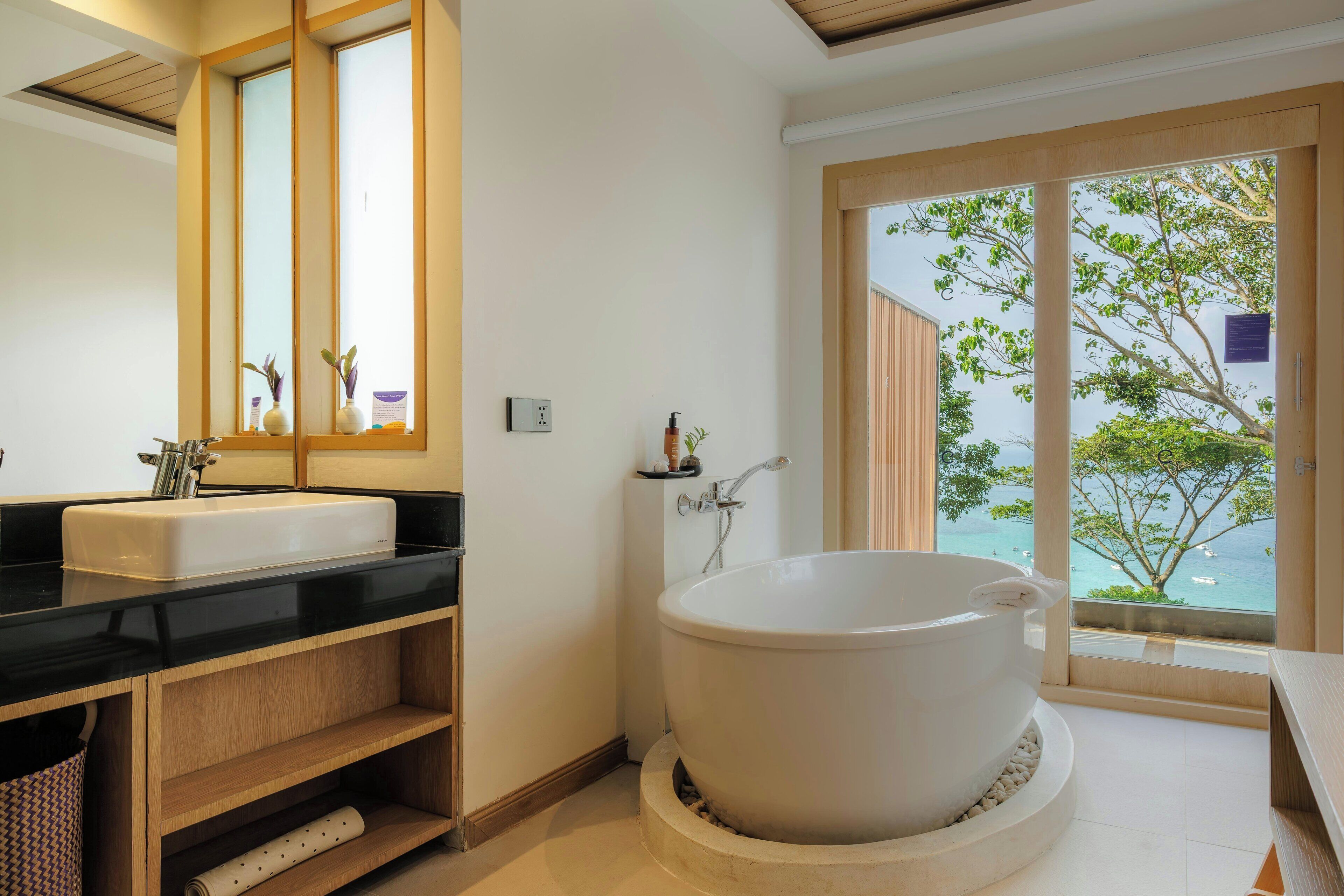 A modern bathroom with a bathtub, a sink, and a large window offering a view of the sea.