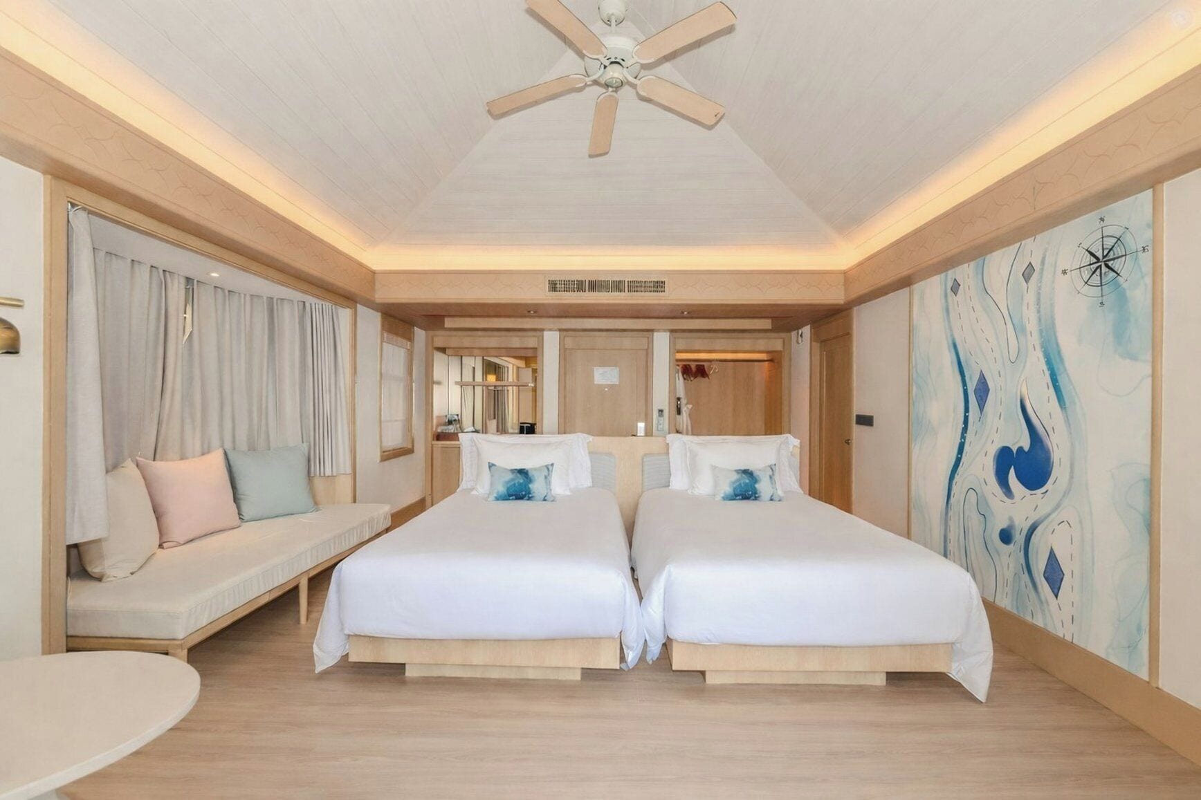 A hotel room with two beds, a ceiling fan, a sofa, and a large abstract painting on the wall.