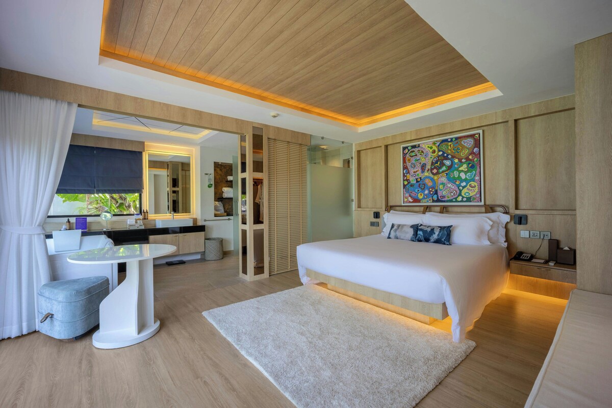 A modern bedroom with a large bed, bedside table, and a desk with a chair.