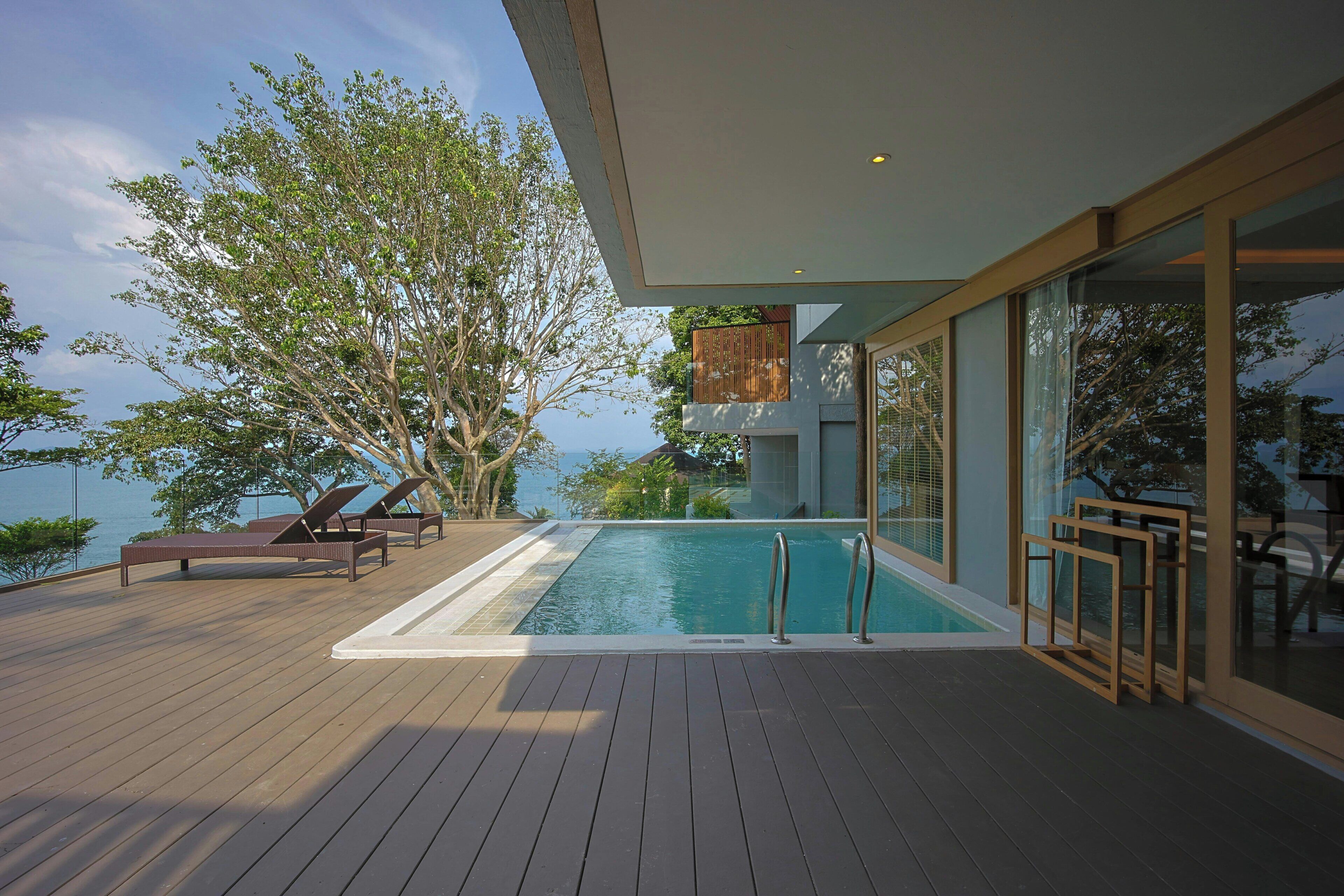 Una terraza de madera con piscina, sillas de descanso y vista al mar.