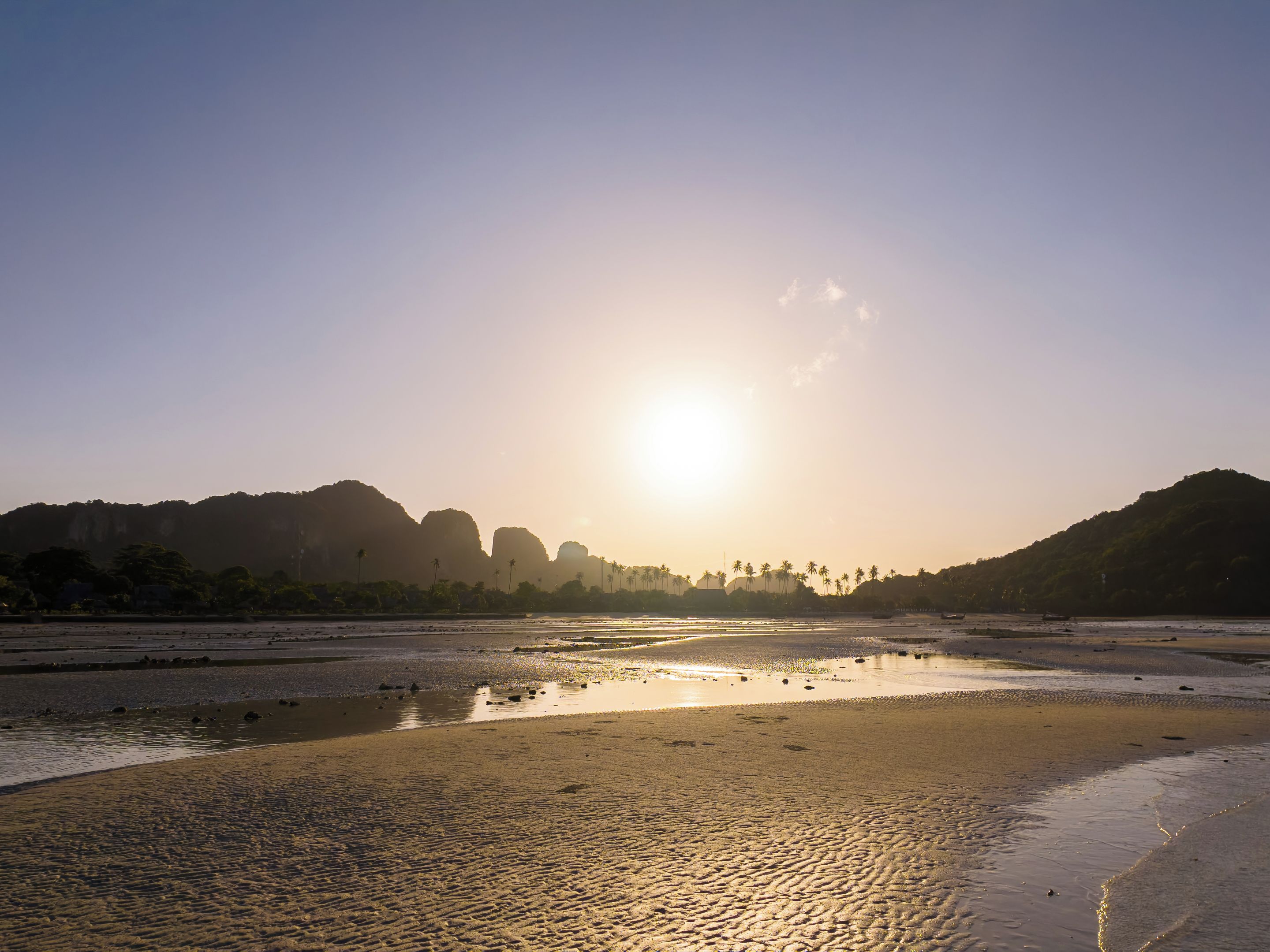 Una playa con cielo despejado y montañas a lo lejos.