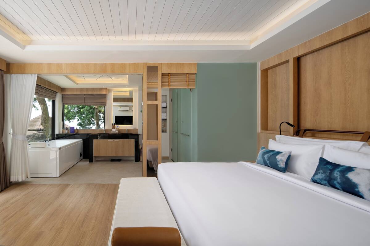 A modern hotel room with a large bed, a desk, and a kitchenette.