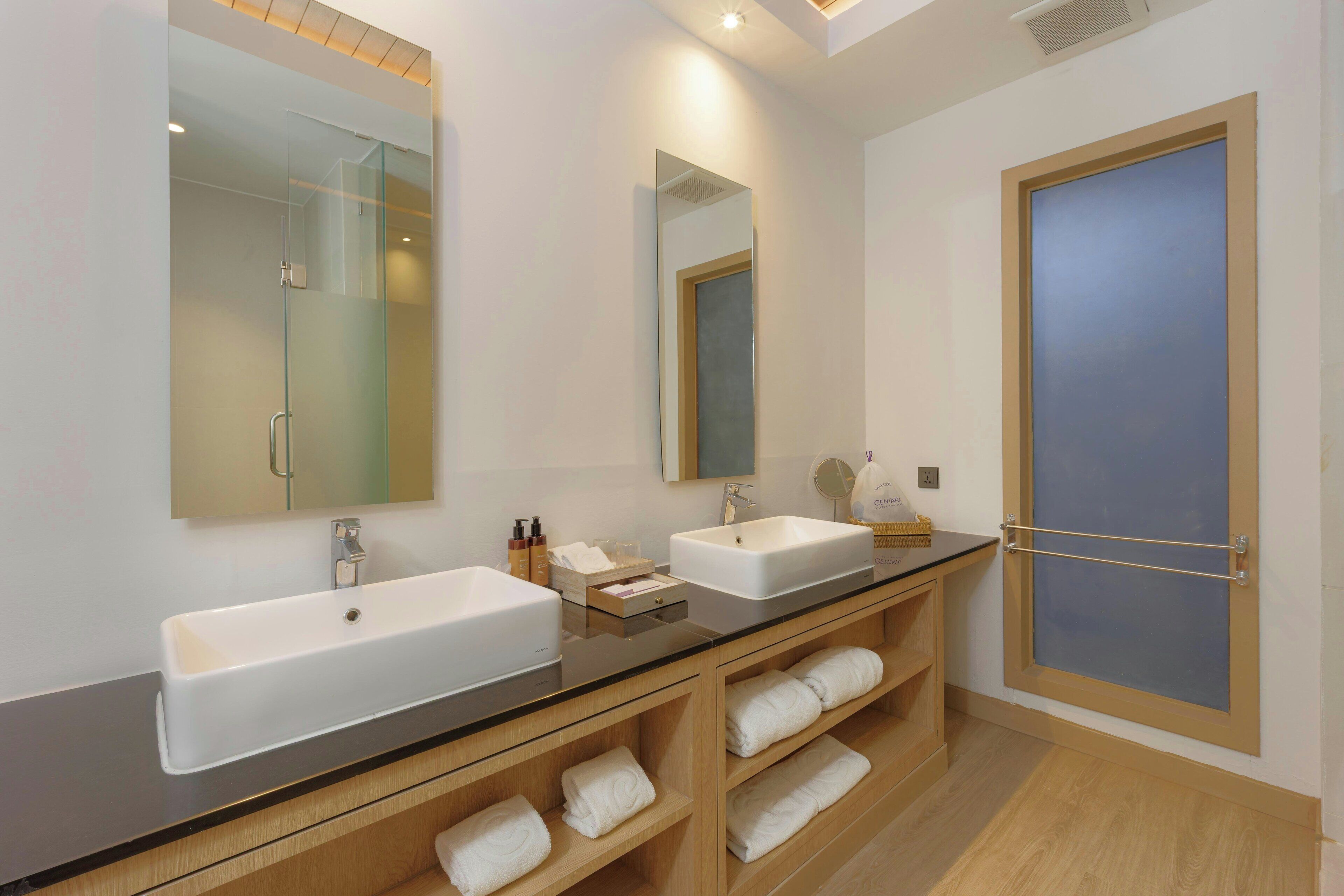 Un baño moderno con dos lavamanos, cabina de ducha de vidrio y tocador de madera con toallas.