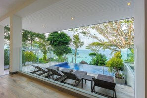 A modern indoor pool area with glass walls, lounge chairs, and a view of the sea. - Centara Villas Phi Phi Island (Ko Phi Phi)