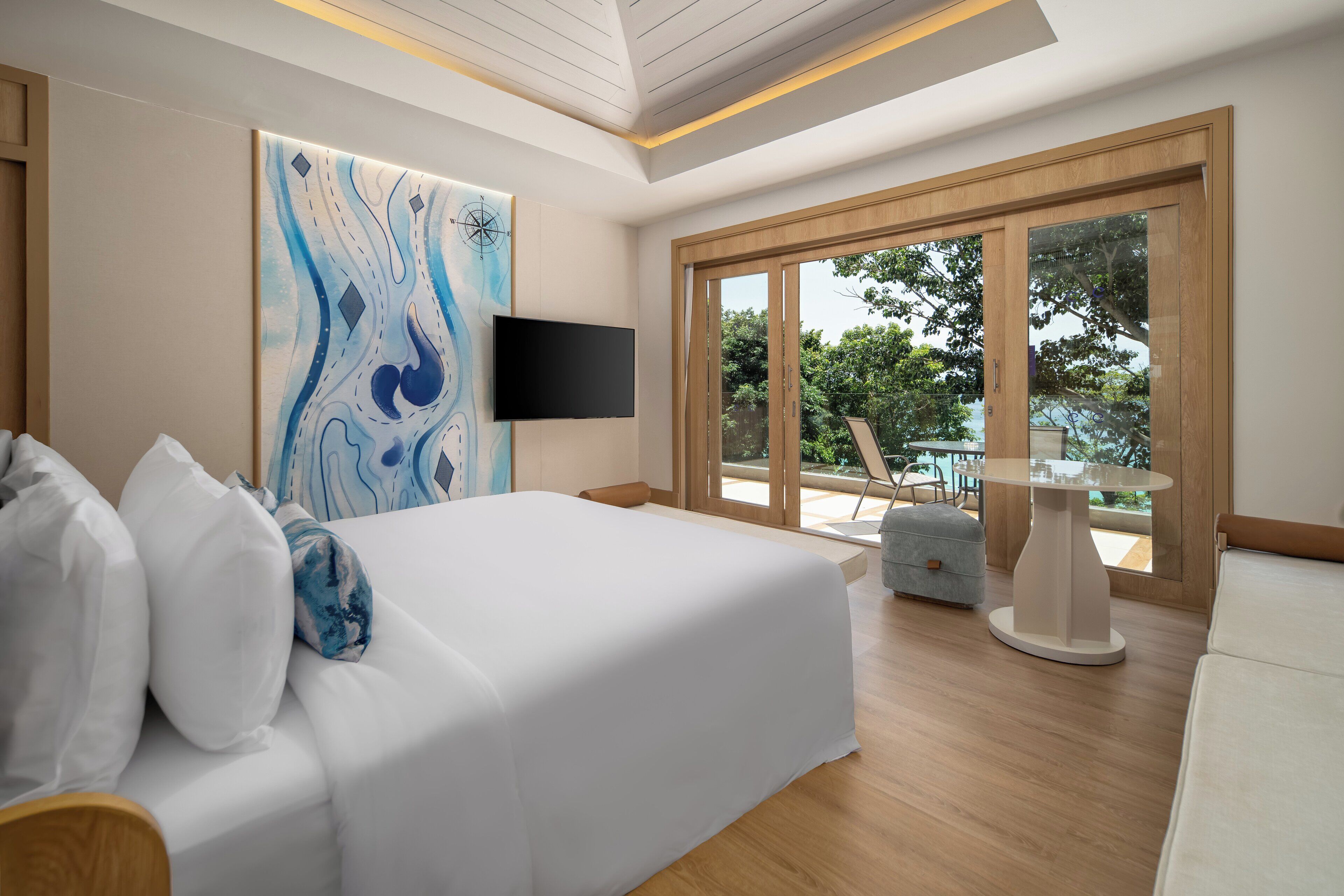 Un dormitorio moderno con una cama grande, televisor de pantalla plana y un balcón con mesa y sillas.