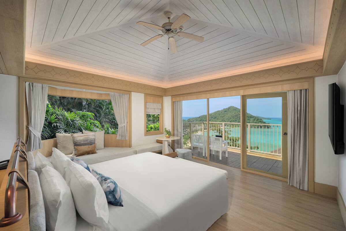 A spacious bedroom with a large bed, a ceiling fan, and a balcony with a view of the ocean.