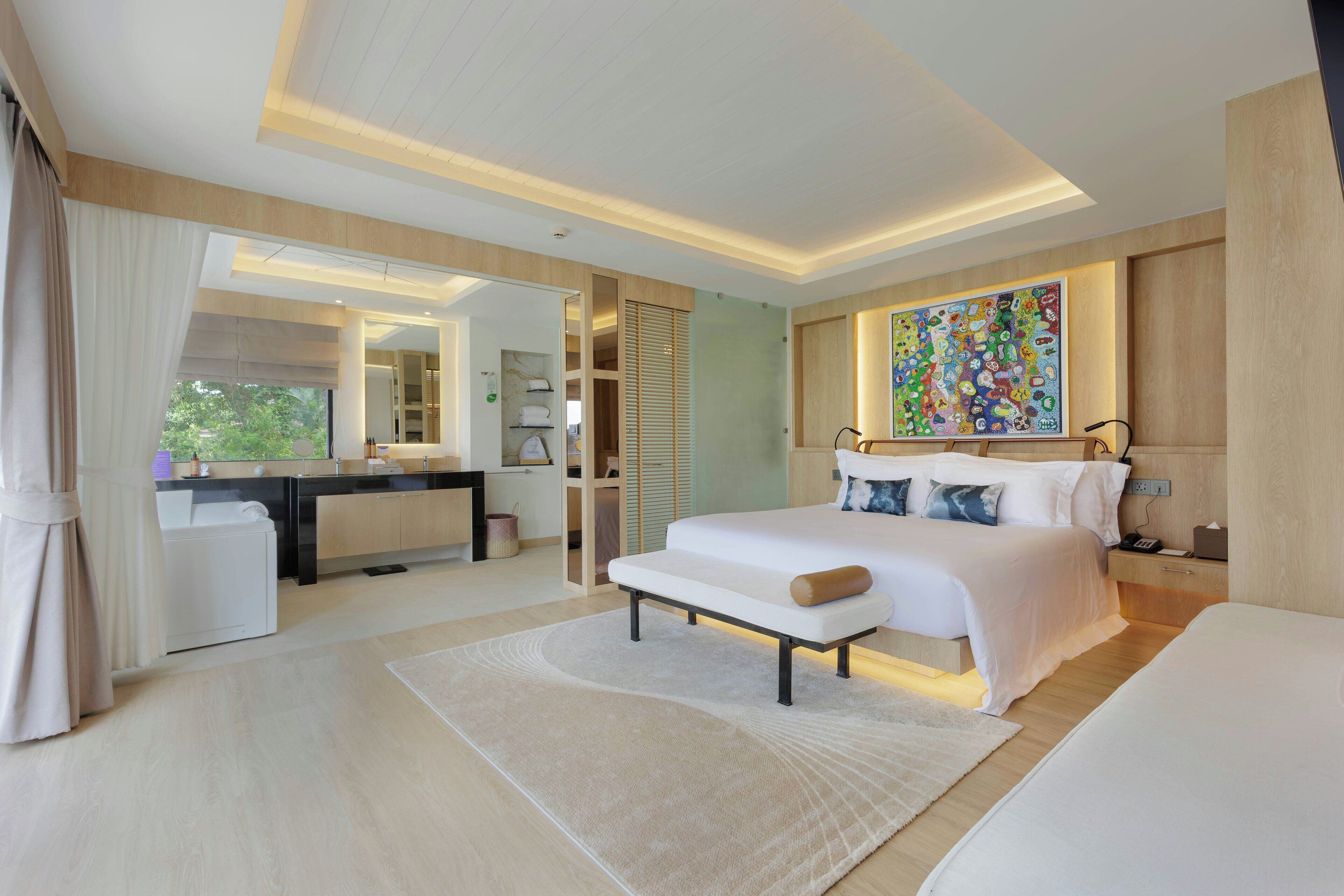 A modern bedroom with a large bed, bedside tables, a desk, and a bathroom visible through an open door.
