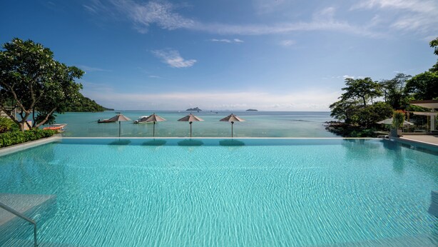 Una piscina azul cristalina con vistas al mar y a islas lejanas.