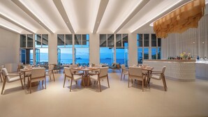 Un comedor moderno con mesas y sillas, ventanas amplias con vista al mar y una zona de bar con botellas.