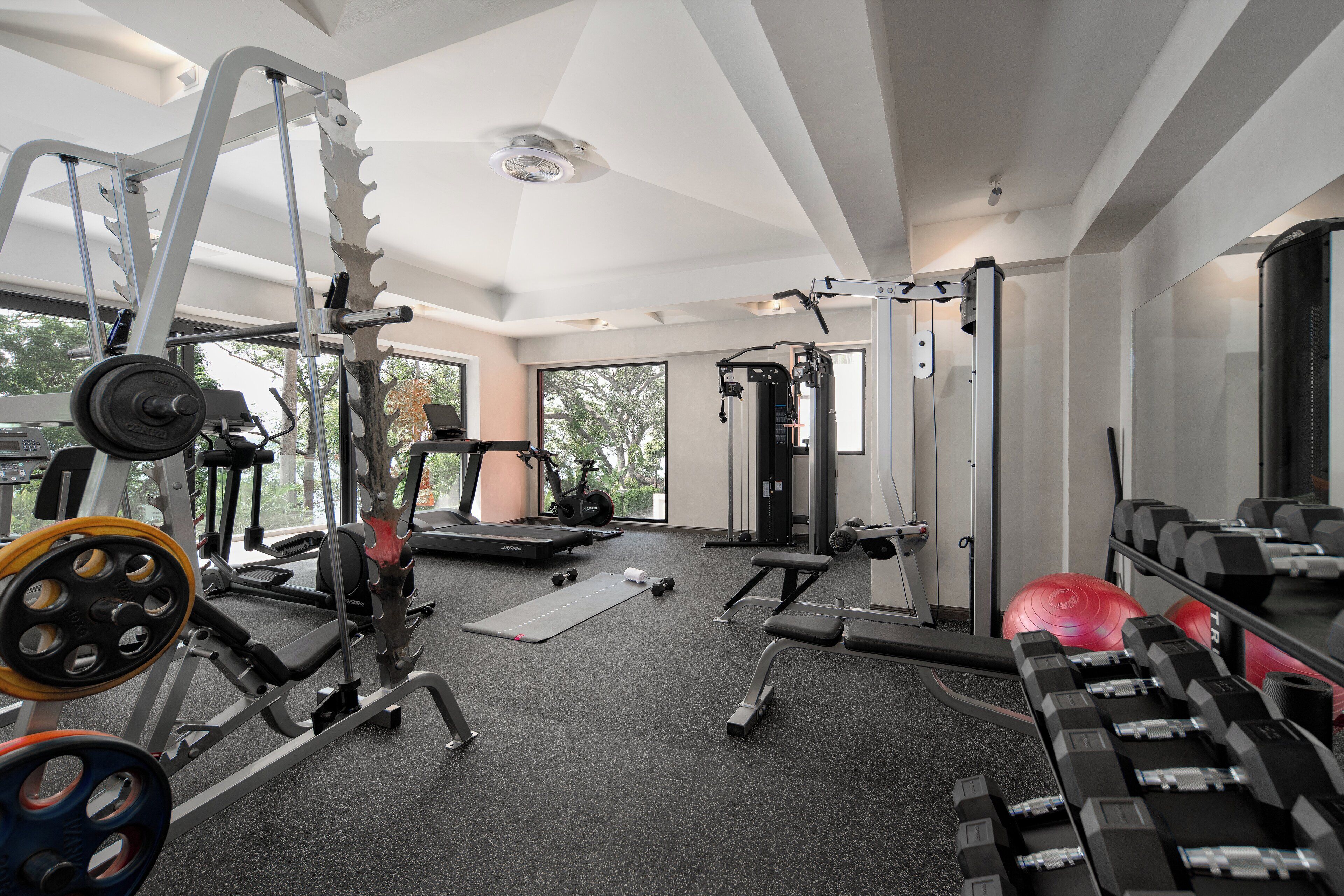 A modern gym with various exercise equipment, large windows, and a spacious layout.