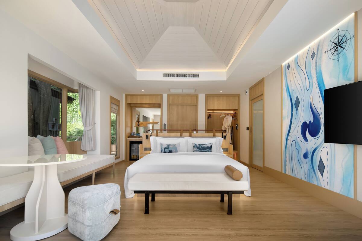 A modern hotel room with a large bed, a seating area, a TV, and a view of the outdoors.