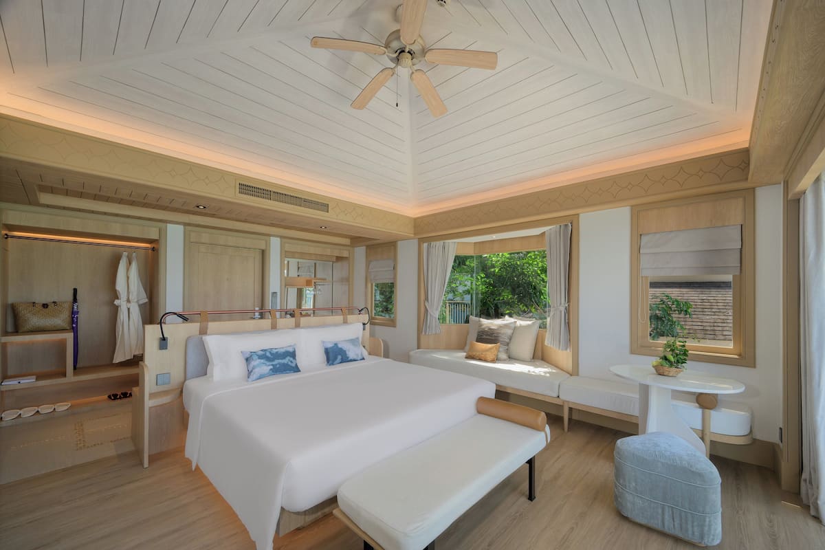 A spacious bedroom with a large bed, a bench, a small table, and a ceiling fan.