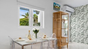 A dining area with a glass table, clear chairs, and a wooden shelf unit. - Tropical Decor Studio  Walk to the Beach  Pool (Noord)