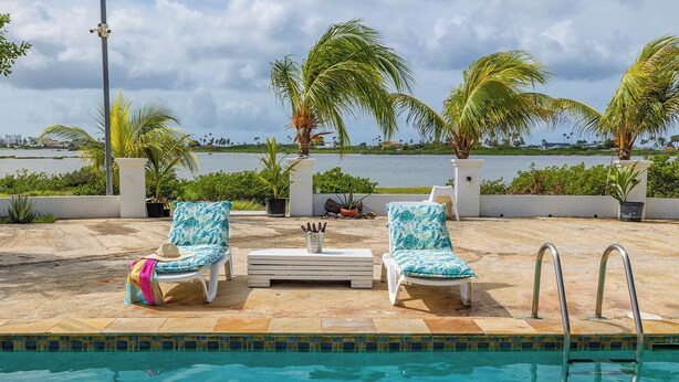 A poolside area with two lounge chairs, a small table, and a pool. - Tropical Decor Studio  Walk to the Beach  Pool (Noord)