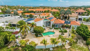A residential area with multiple houses, a swimming pool, and solar panels on rooftops. - Tropical Decor Studio  Walk to the Beach  Pool (Noord)