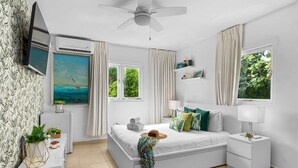 A bedroom with a bed, bedside tables, a TV, a ceiling fan, and a window with curtains. - Tropical Decor Studio  Walk to the Beach  Pool (Noord)