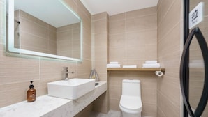 A modern bathroom with a white sink, a mirror, a toilet, and a shelf with towels. - Dalian Youxi-ChengYuan Hotel (Dalian)